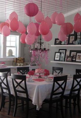 a dining room table with pink balloons hanging from the ceiling and pictures on the wall