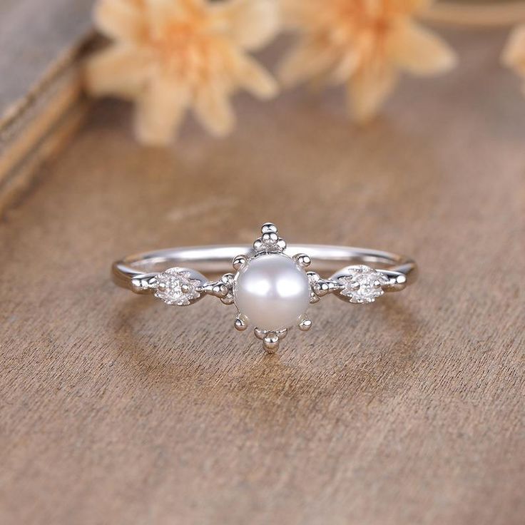 a white pearl and diamond ring sitting on top of a wooden table next to flowers