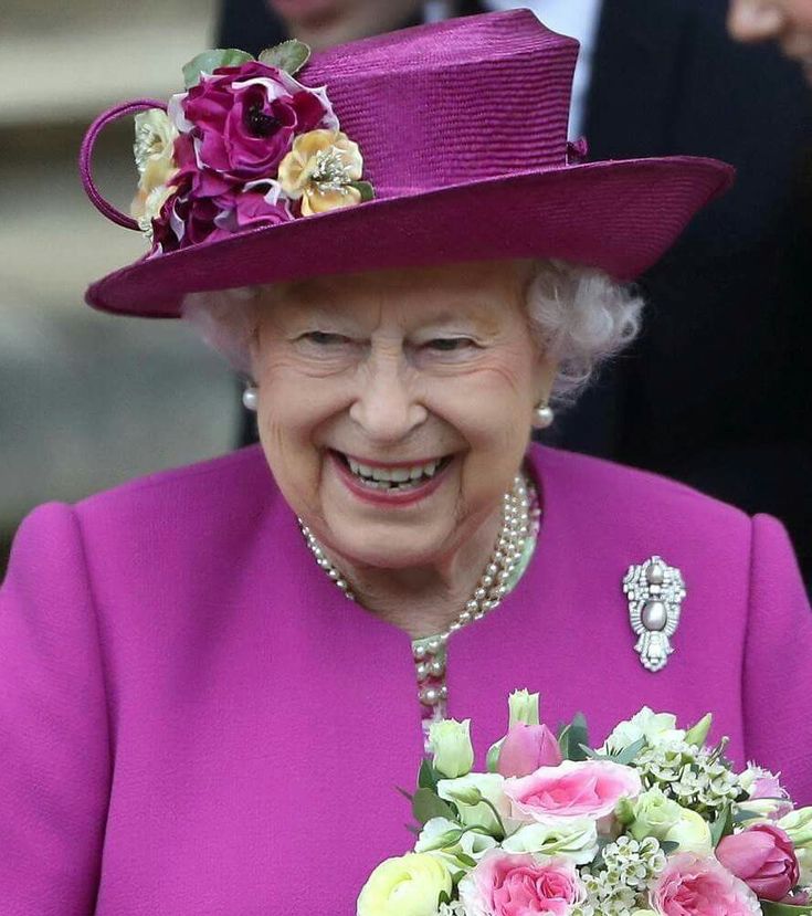 the queen smiles as she holds a bouquet of flowers