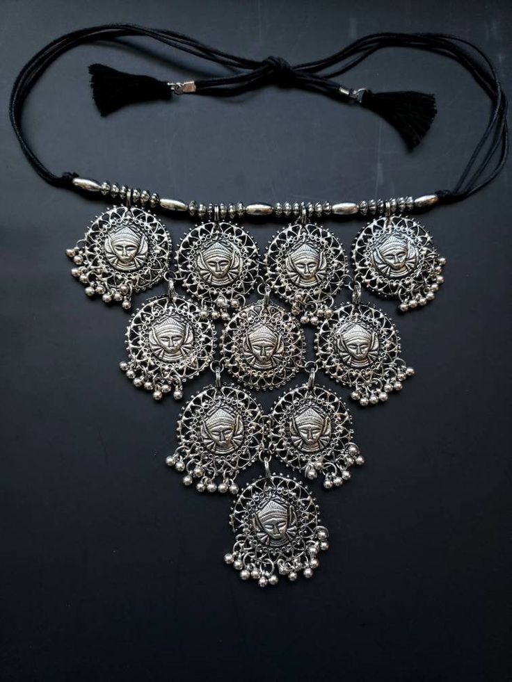 Stunning India bib necklace of Hindu goddess Durga. What makes this necklace standout is the eye catching row of beads along the neckline, and the perfect overall symmetry of the hanging design. And how great it looks on a simple blouse or dress. Perfect tucked inside an open collar shirt. Detailed 3D portrait of goddess, surrounded by a heart motif picture frame. Little bells suspended move when you move, adding to the allure. In oxidized silver to reveal the details of the face. Polished to a Bohemian Bib Necklace For Wedding, Spiritual Festival Choker Necklace, Silver Bohemian Dangle Choker, Silver Dangle Bohemian Choker, Spiritual Choker Necklaces For Festivals, Festive Silver Choker Necklace, Bohemian Necklaces With Intricate Design For Festivals, Silver Metal Spiritual Choker, Silver Spiritual Metal Choker