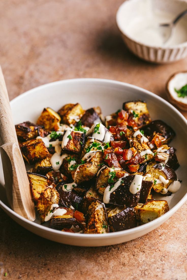 a white bowl filled with cooked potatoes covered in ranch dressing next to a wooden spoon