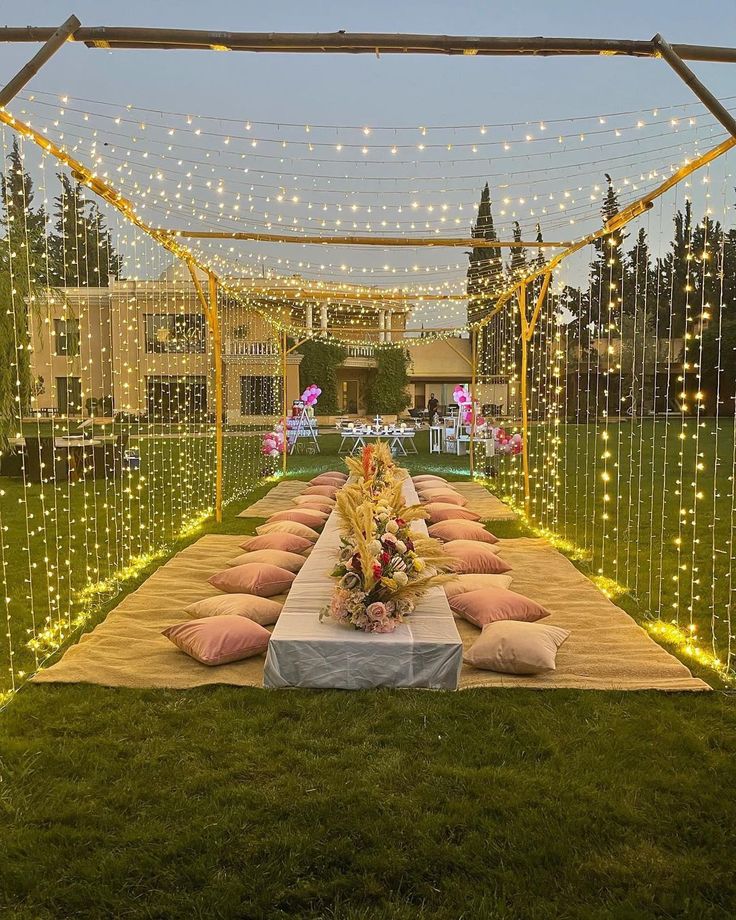 a long table with pillows on it in the middle of an outdoor area decorated with fairy lights