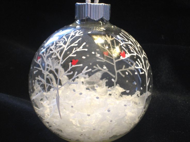 a glass ornament with snow and red berries on it's top, hanging from a black background