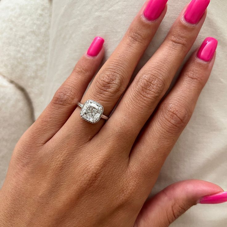 a woman's hand with pink nail polish and a diamond ring on her finger