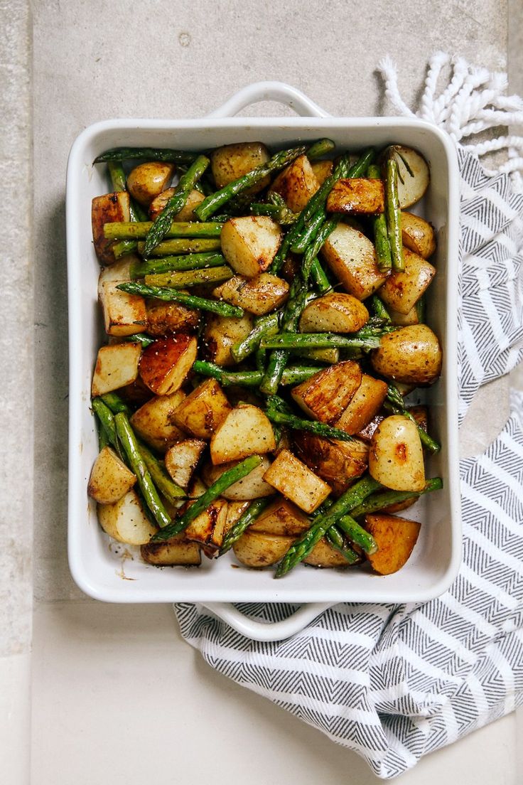 a white dish filled with potatoes and asparagus