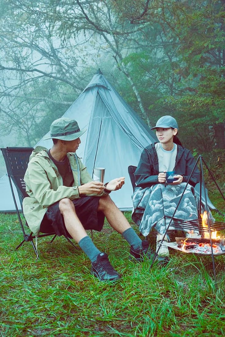 two people sitting in chairs next to a campfire