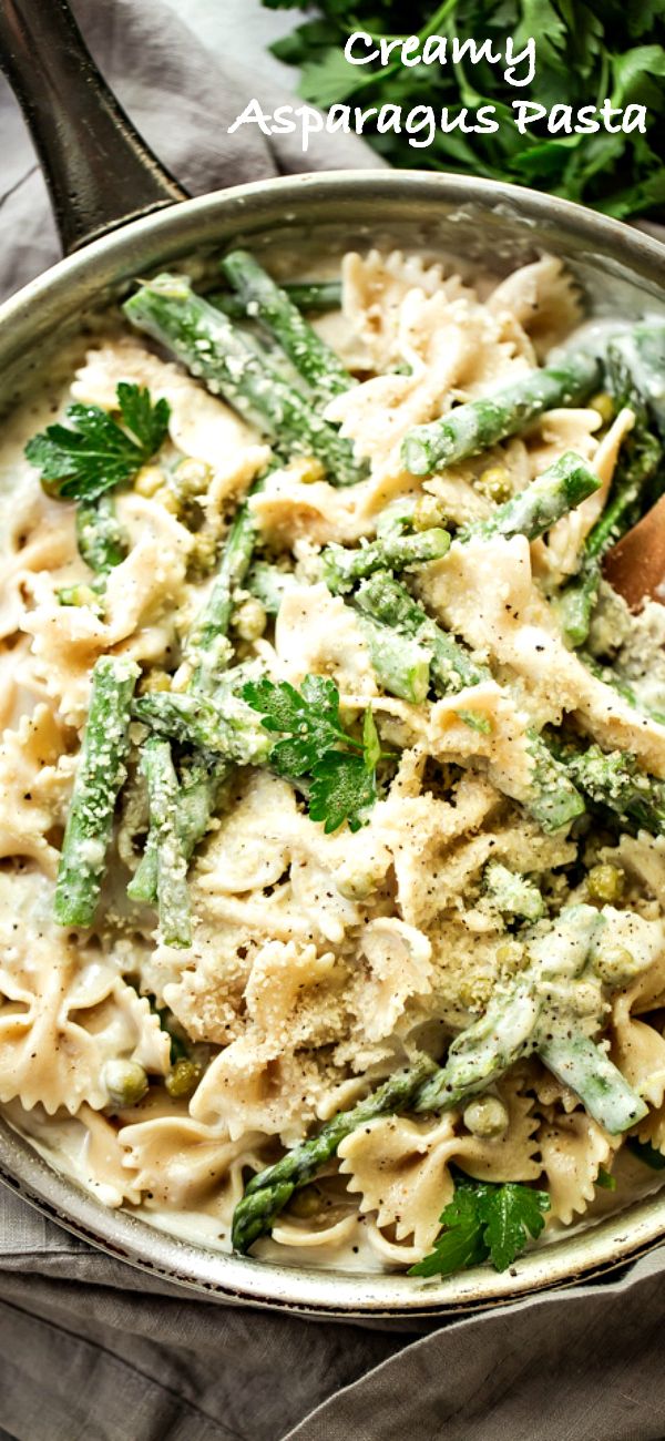 a pan filled with pasta and asparagus on top of a table next to a wooden spoon