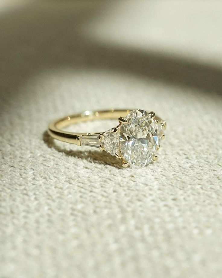 a diamond ring sitting on top of a white cloth covered floor next to a window