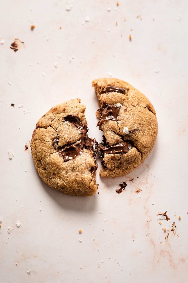 two chocolate chip cookies split in half on top of a white surface with bits missing