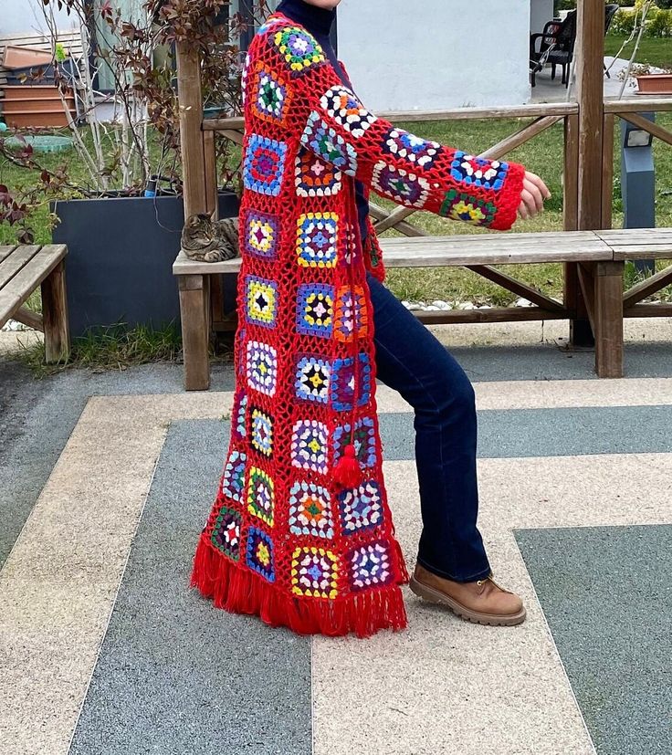 a woman wearing a red crocheted coat and jeans