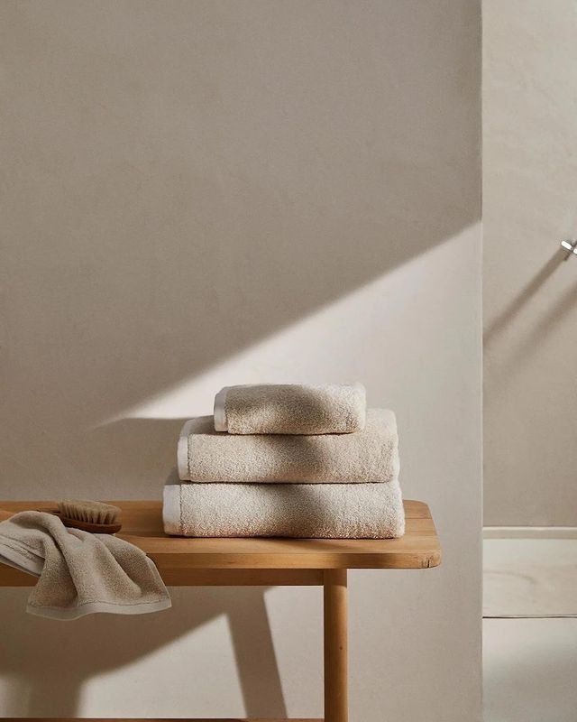 three towels stacked on top of a wooden table next to a wall with a lamp