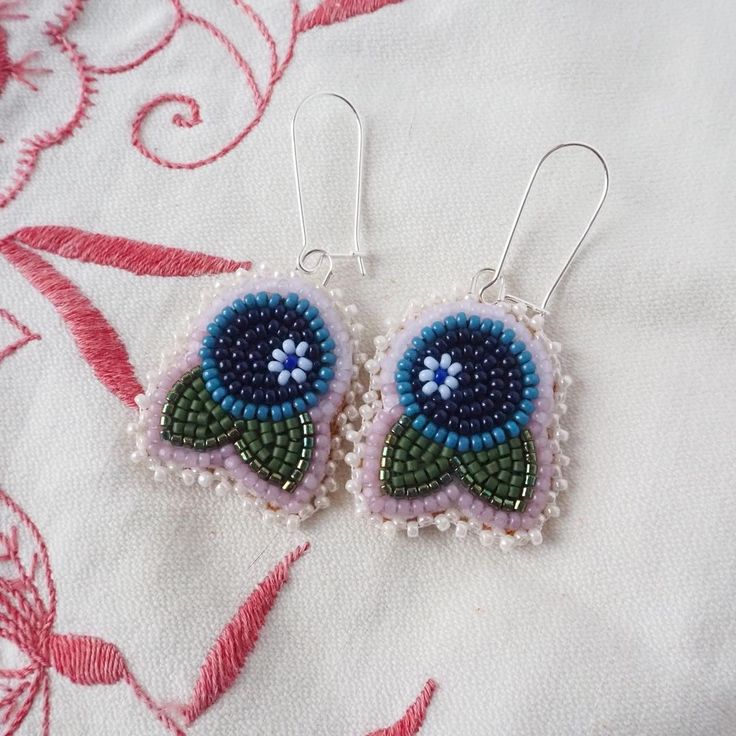 a pair of blue and green beaded earrings sitting on top of a white cloth