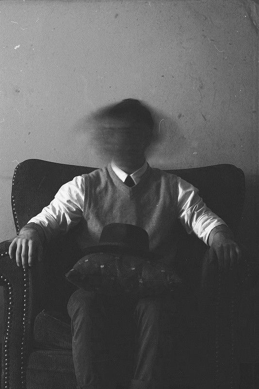 a man sitting on top of a chair with a hat in his hand and the shadow of him