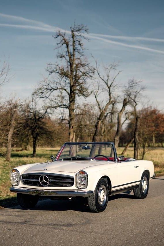 an old mercedes benz is parked on the side of the road in front of some trees