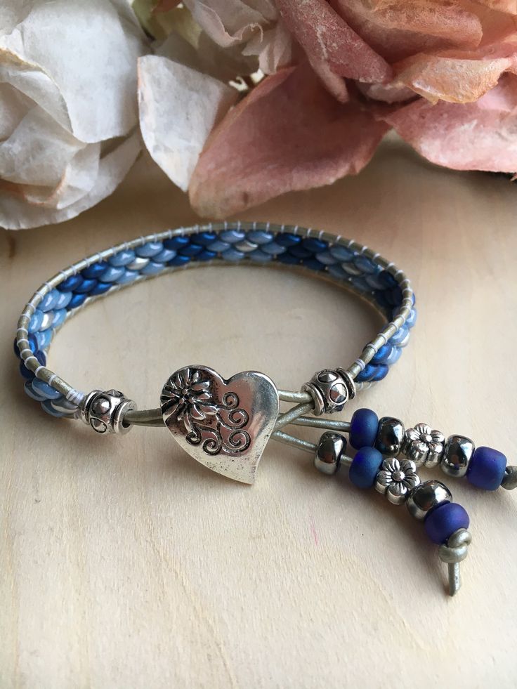 Beaded Leather Blue n Gray Heart Wrap Bracelet  The length listed is the inside circumference when the bracelet is clasped. This Bracelets Features Genuine Round Gray Leather 1.5mm 17x18mm Silver Metal Heart Button  Blues and Gray Superduos (2 hole) beads This Bracelet is so comfortable to wear it will really surprise you, and an excellent addition to any outfit! All Bracelets are hand made and created with love and joy. The Blues and Grays of this bracelet blend together so nicely with the Gray leather, and are hand stitched in a Floral Design. Your new Treasure will arrive gift wrapped whether you are buying it for yourself or a loved one, along with care instructions. To determine the size bracelet for you, measure your wrist just below the wrist bone, THEN ADD 1/4"-1/2" according to yo Blue Cuff Bracelet, Gray Heart, Beaded Leather Bracelet, Super Duo, Beaded Wrap Bracelets, Heart Button, Bracelet Leather, Metal Heart, Beaded Wraps