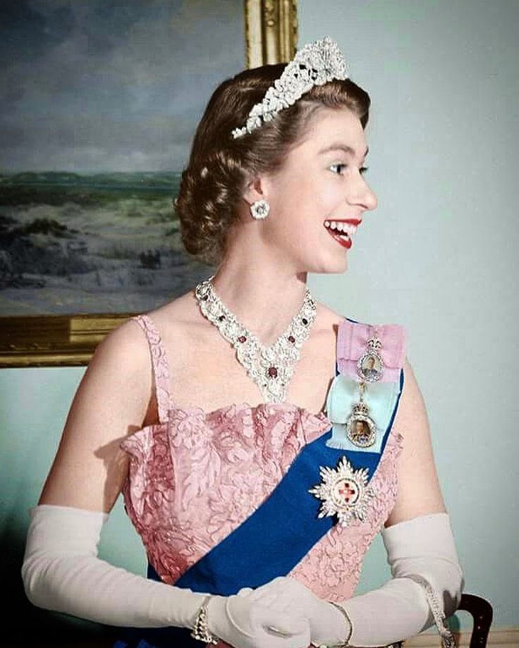 a woman in a pink dress and tiara standing next to a painting on the wall