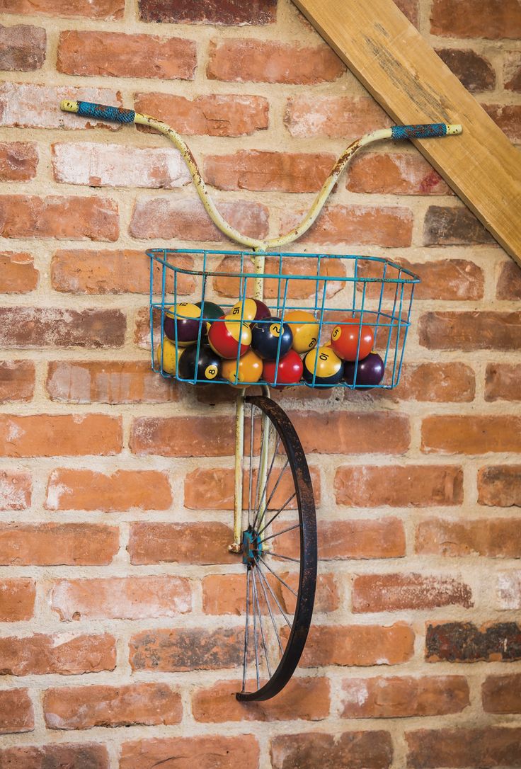 an old bicycle wheel is mounted to a brick wall with balls in the basket on it