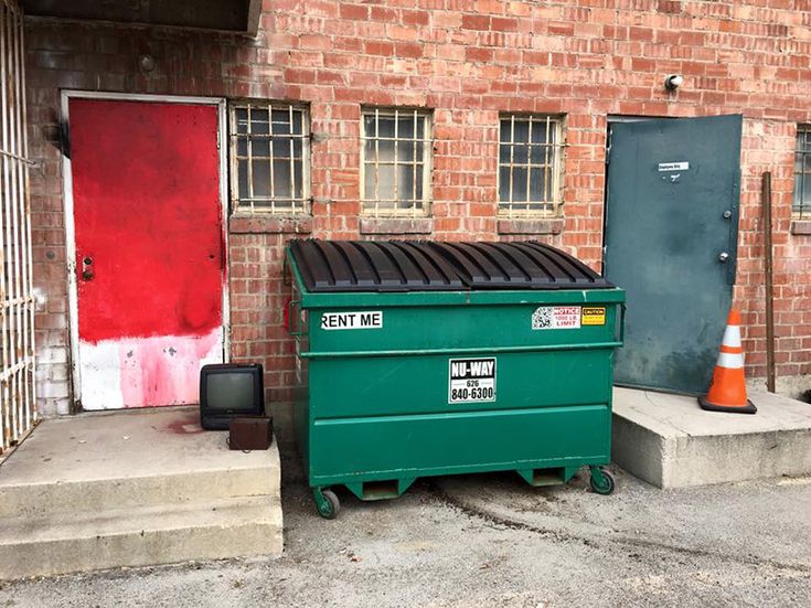 a green dumpster sitting in front of a brick building next to a red door