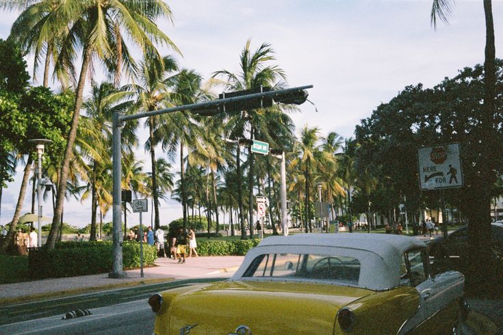 an old yellow car is parked on the side of the road in front of palm trees