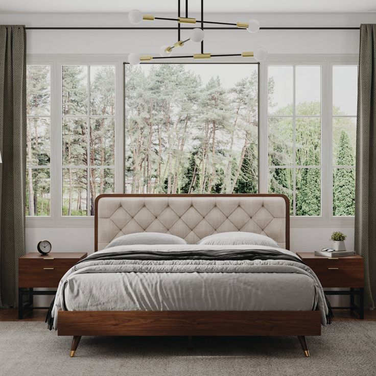 a bedroom with a bed, nightstands and windows in front of the window are trees