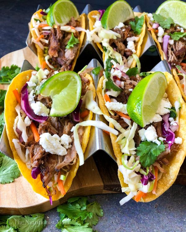 several tacos with meat, cabbage and limes on a cutting board next to cilantro