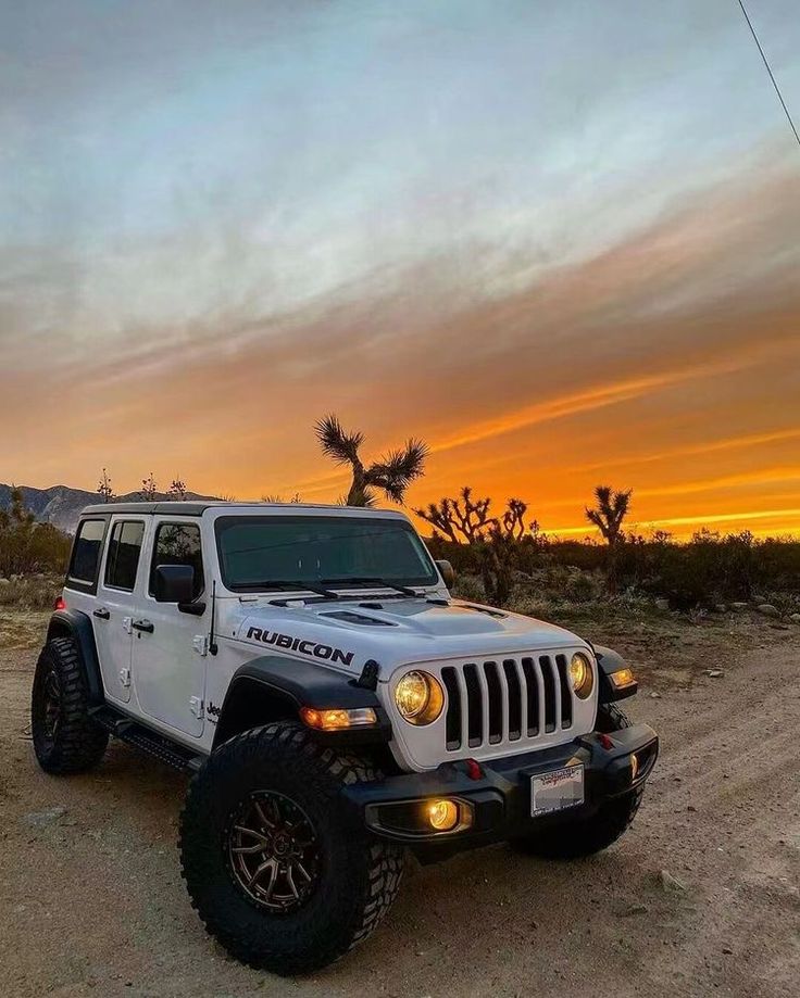 a white jeep parked in the desert at sunset