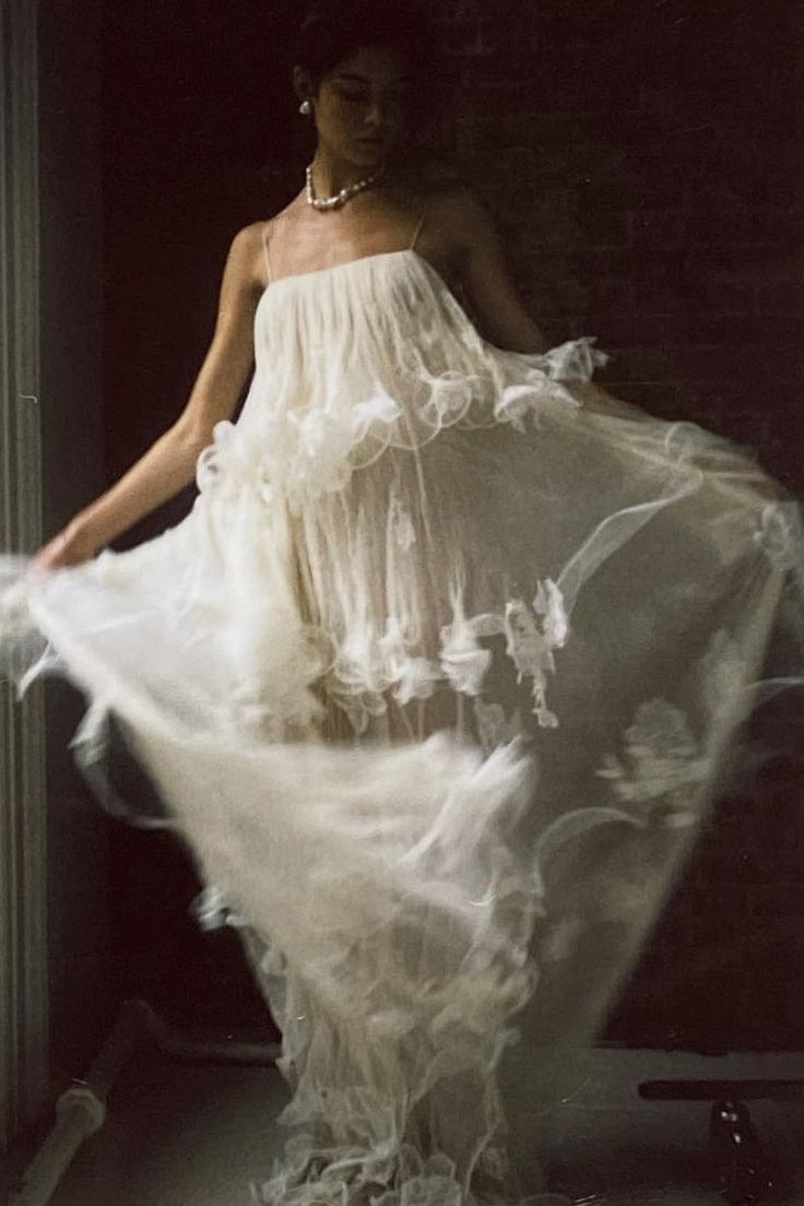 a woman is standing in front of a window with her dress blowing in the wind