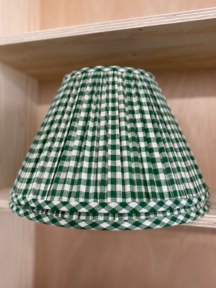 a green and white gingham lamp shade hanging from a wooden shelf in a room