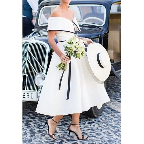 a woman in a white dress and hat is standing next to an old fashioned car