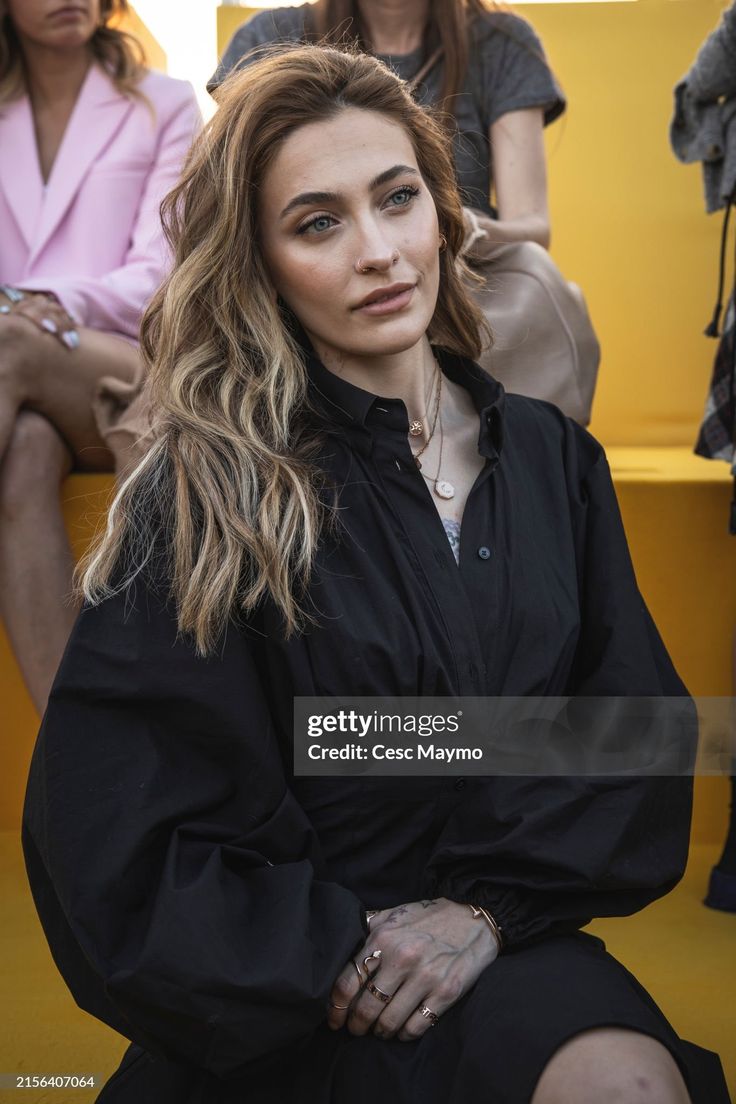 a woman sitting on a bench in front of other people at a fashion show stock photo