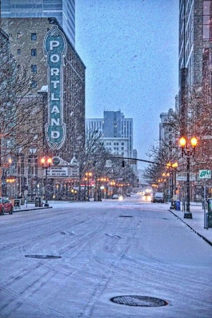 an empty city street with snow on the ground and buildings in the backgroud