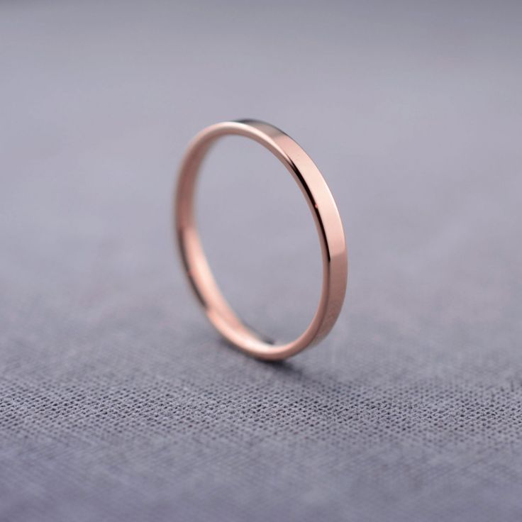 a thin rose gold wedding ring sitting on top of a gray cloth covered tablecloth