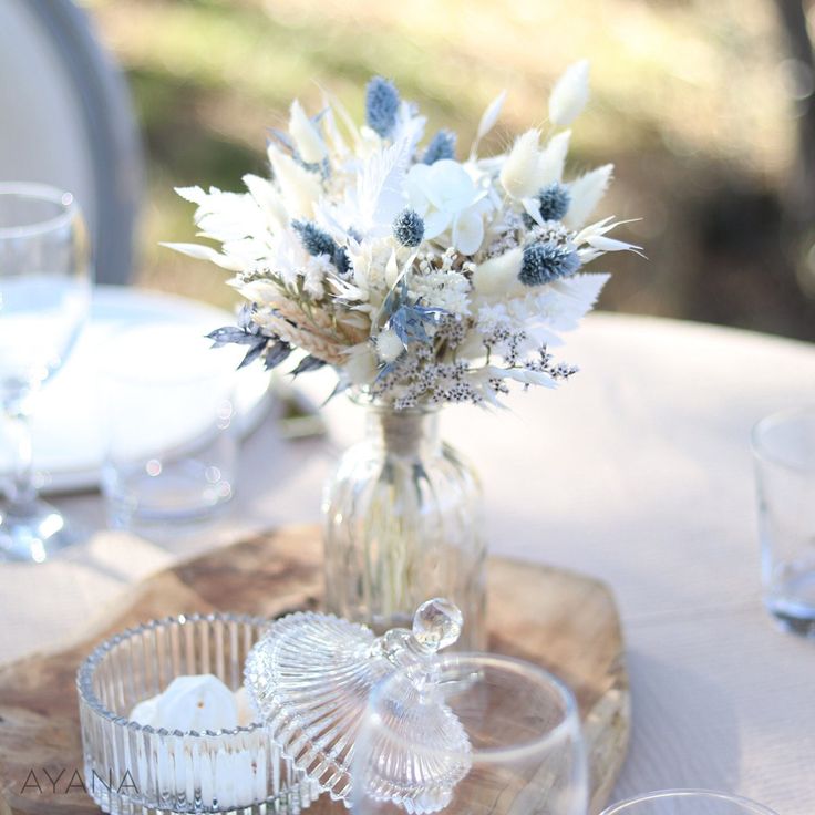 there is a vase with flowers in it sitting on a wooden tray next to wine glasses