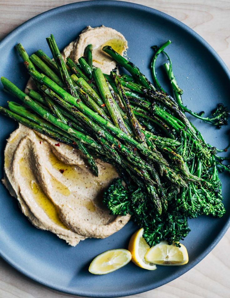 asparagus and hummus on a blue plate with lemon wedges next to it