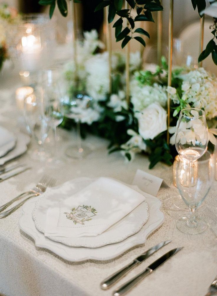 the table is set with silverware and white flowers in vases, candles, and napkins