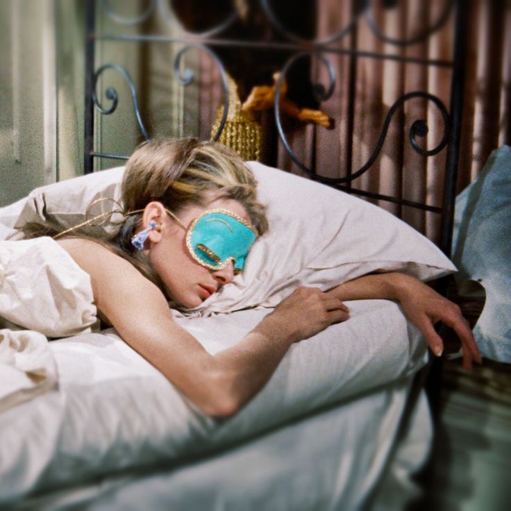 a woman laying in bed with her eyes closed and blind folded over her eyeglasses