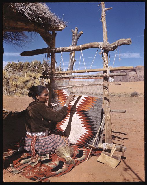 a woman sitting on the ground next to an old weaving loom with her hands