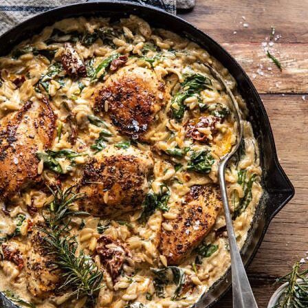 a skillet filled with chicken and pasta on top of a wooden table next to a fork