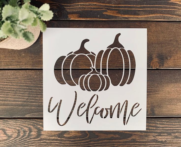 a sign that says welcome with pumpkins on it next to a potted plant