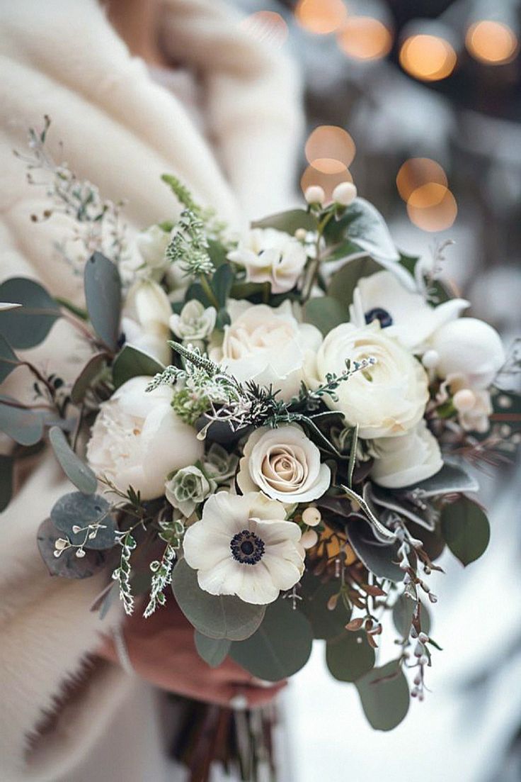 a bridal bouquet with white flowers and greenery is held by a woman in a fur coat