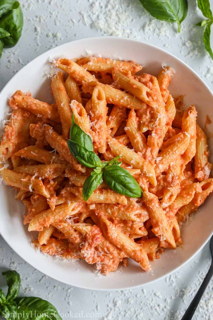 pasta with basil and parmesan cheese in a white bowl on a marble table