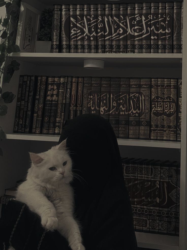 a white cat sitting on the arm of a person in front of bookshelves