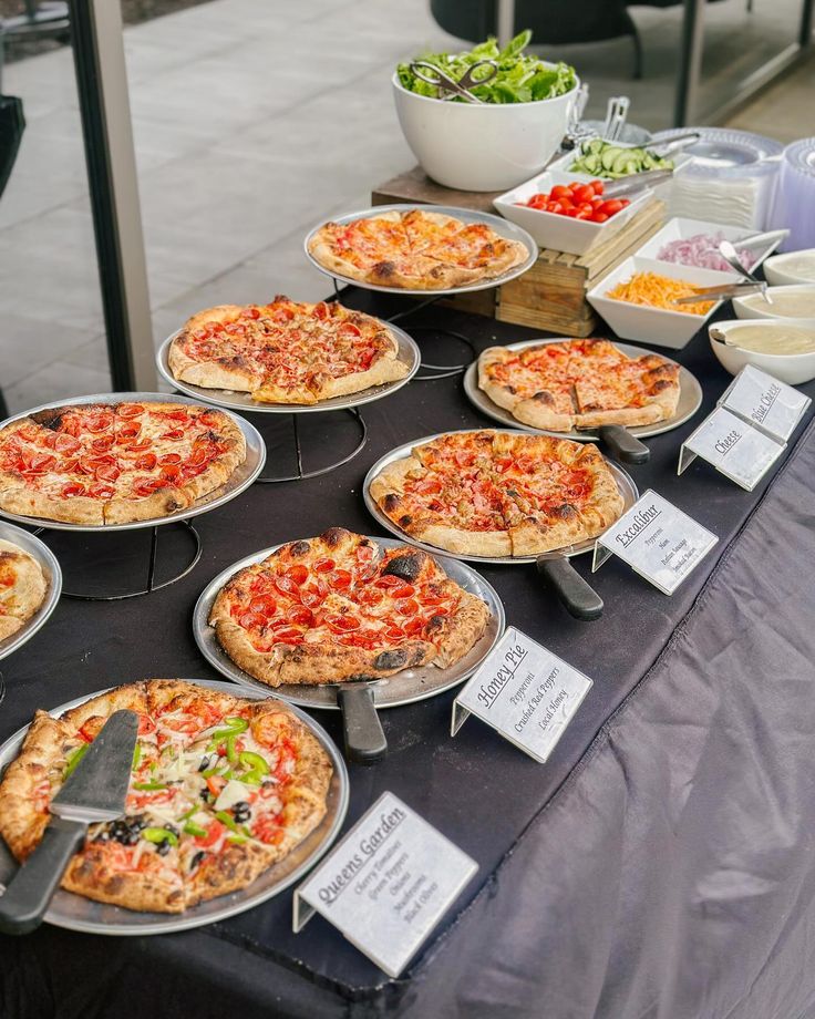 a table topped with lots of pizzas and bowls of salad on top of it