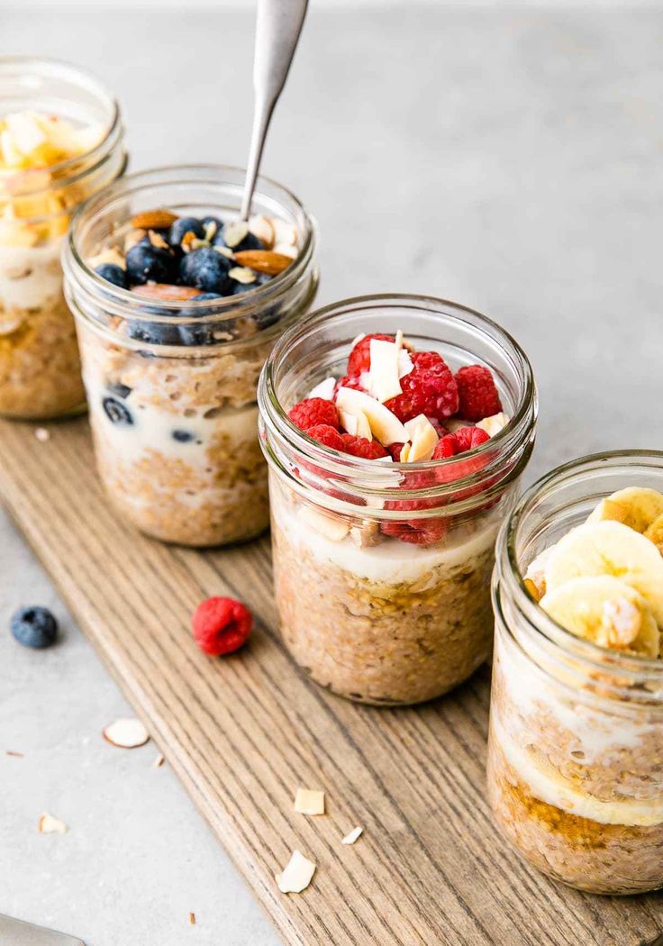 three mason jars filled with oatmeal, bananas and blueberries on a cutting board