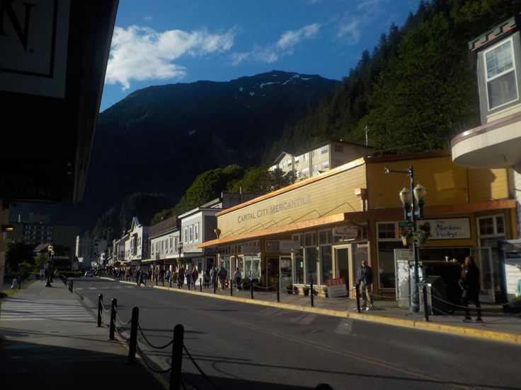 people are walking down the street in front of shops and buildings with mountains in the background