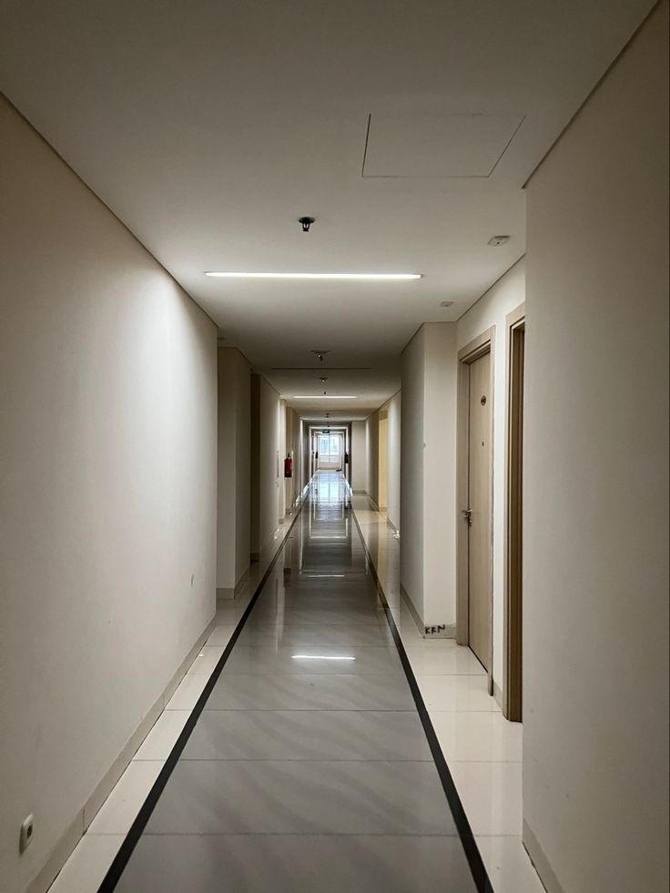 an empty long hallway with white walls and black lines on the floor is lit by recessed lights