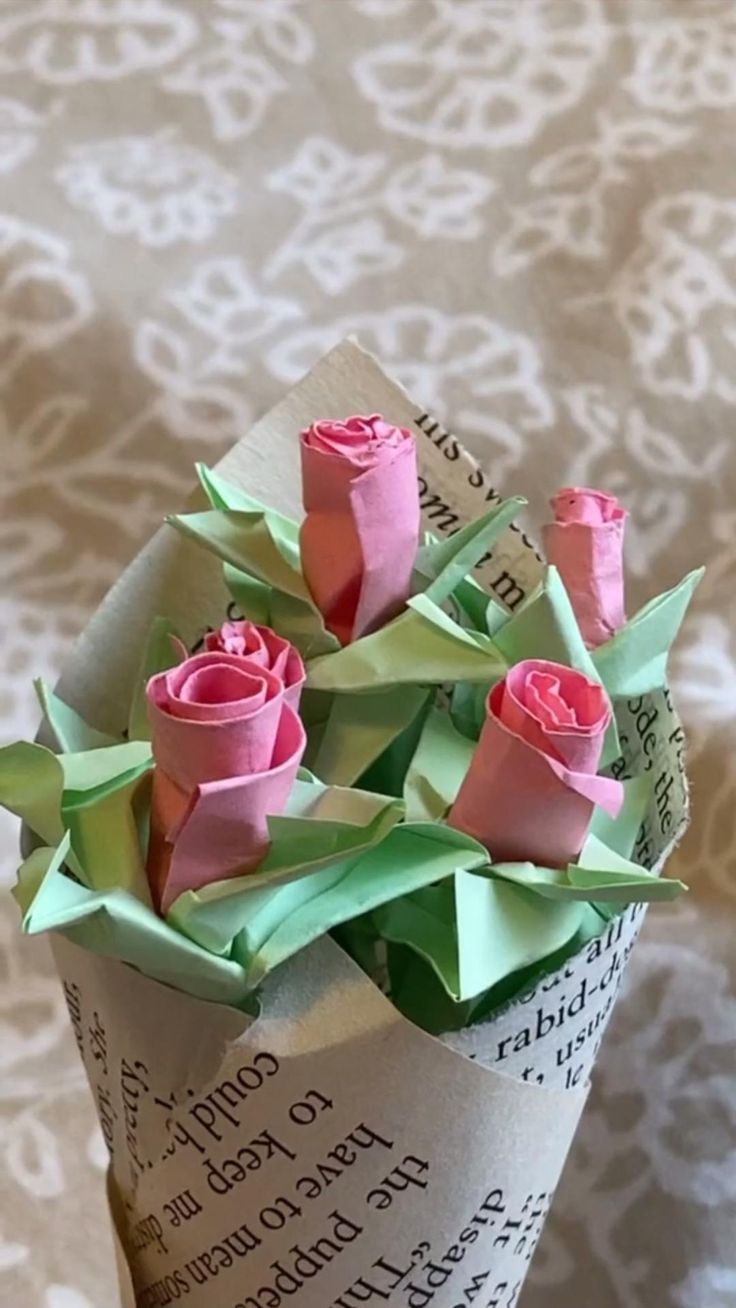 origami roses in a paper vase on a tablecloth covered surface with an old book page