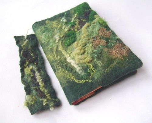 an old book covered in green and brown fabric next to a pair of scissors on a white surface