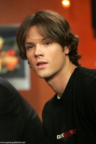 a young man with long hair is looking at the camera while wearing a black shirt