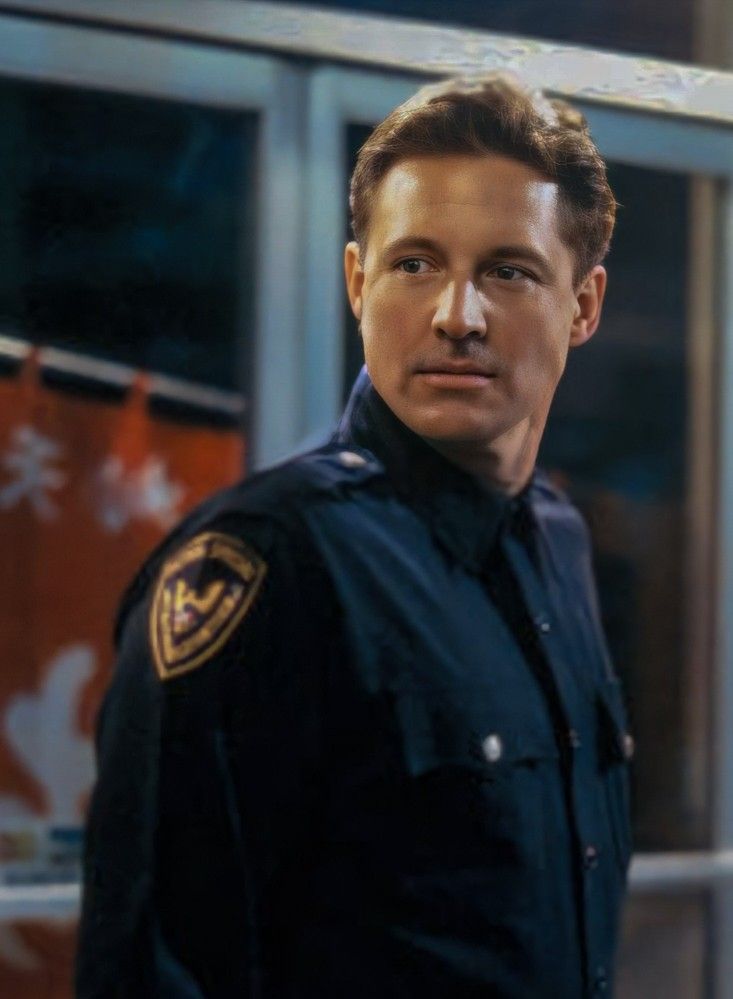 a police officer standing in front of a window with his hand on his hip and looking at the camera